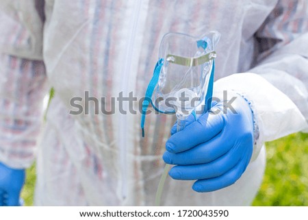 Close up picture of man's hand, wearing hazmat suit and gloves, holding an oxygen mask