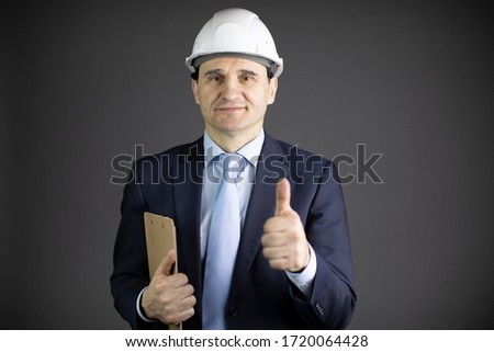 Handsome chief engineer in hard hat with clipboard showing like sign with thumb up isolated on grey background. Successful man from industrial sphere, oil refinery industry concept