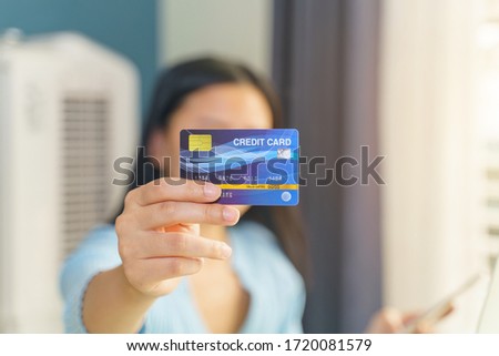 Woman holding blue mock up credit card while using smartphone at home.Shopping and payment online.
