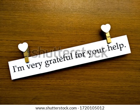 The sentence "I'm very grateful for your help." in a white paper with white heart shapes and wooden pattern background.
