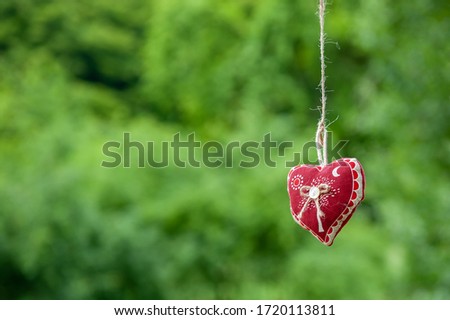 Isolated handmade cotton fabric heart hanging on bast string on green grass background. Red fabric heart hanging on the clothesline. Summer wedding theme. Love and valentine in nature.