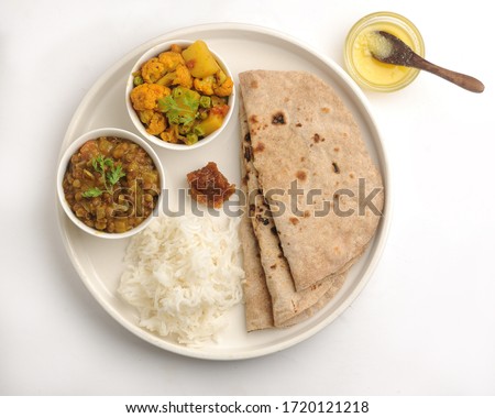 Veg Thali or Vegetarian Indian food plate with roti or flat bread, ghee butter, lemon pickle, rice, cauliflower curry and daal or lentil Royalty-Free Stock Photo #1720121218