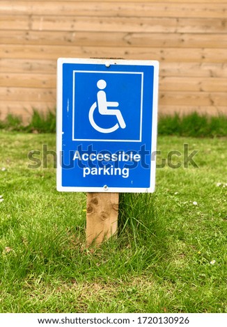 Accessible parking sign in grass and a wooden fence background. The sign shows a wheelchair on a blue background.