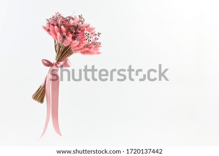 Small bouquet of pink dried flowers knitted with a pink satin ribbon on a white background, copy space.