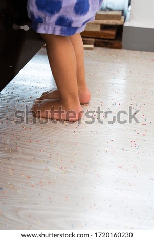 Colourful Sugar sprinkles, decoration on the wooden floor with a child foot stepping on. Messy and scattered. Childhood concept.