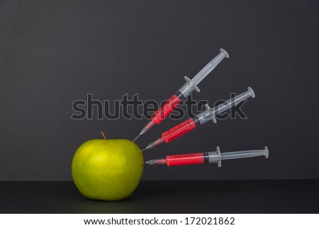Red liquid in the syringe injected into green apple