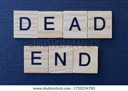 phrase from gray words dead end of small square wooden letters on a black background