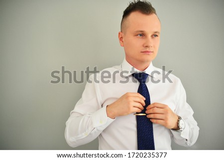 People, business, fashion and clothing concept - close up of man in shirt dressing up and adjusting tie on neck at home. Gray background.
