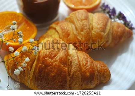 Breakfast: Croissants on a white plate with flowers and oranges.