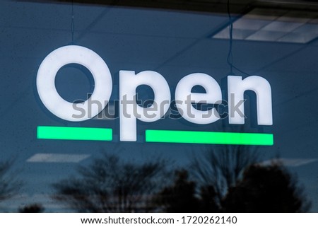 Open sign in white text and green light underline hanging in a storefront window.