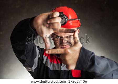 Portrait of coal miner looking through a finger frame against a dark background