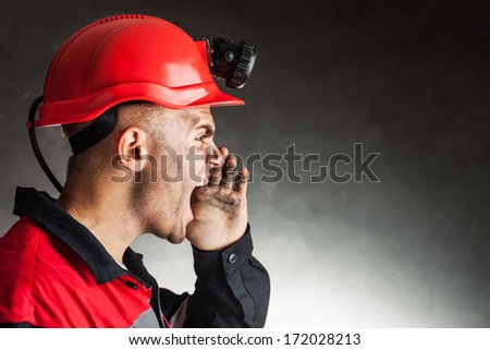Side view portrait of angry coal miner shouting against a dark background