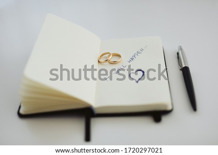Notebook with white pages and message. white background. It will happen is the message. weeding rings and pen in image.