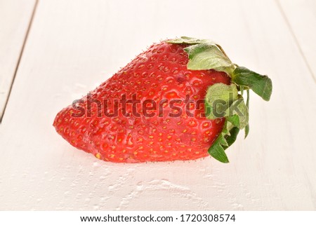 One large strawberry, close-up, on a painted wooden table.