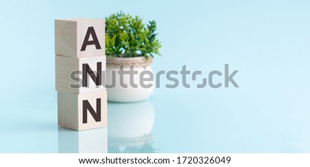 Ann-text on wooden cubes, on a blue background. In the background, a green plant in a white pot. Reflection in a mirror surface