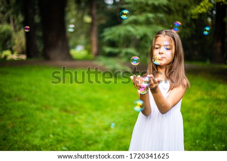 Cute small girl playing with soap bubbles in nature