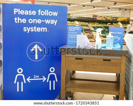 'Please follow the one way system' sign in grocery store in the UK next to disinfectant for trolleys illustrating concept of safety precautions in Uk during the coronavirus pandemic