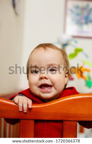 little child girl in a red sweater, smiles beautifully, in a crib, plays and has fun, emotional photo
