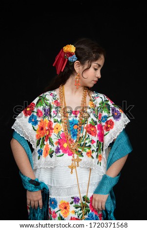 Latina teenager Mexican, dancer with typical costume from Yucatan Mexico, with black background, costume model embroidered with flowers in cross stitch handmade, with gold chains and coral beads