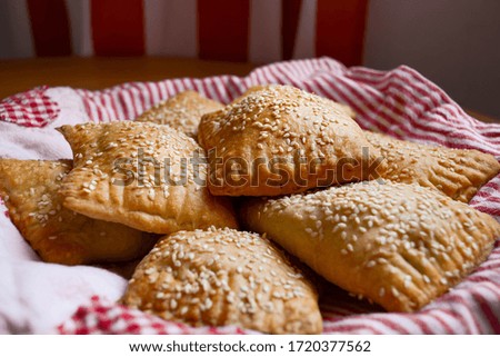 Puff pastry pies with spinach filling and sesame seeds on top on a textile lining in red and white stripes.