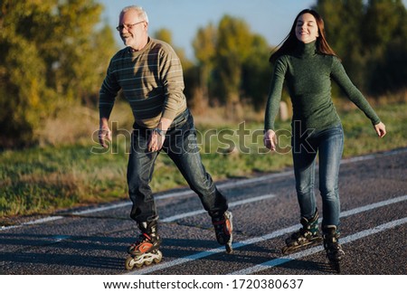Parents and children spend time together. Older generation and sport. Active lifestyle of the pensioner. Happy old man riding on rollers with his daughter on the road in autumn park.