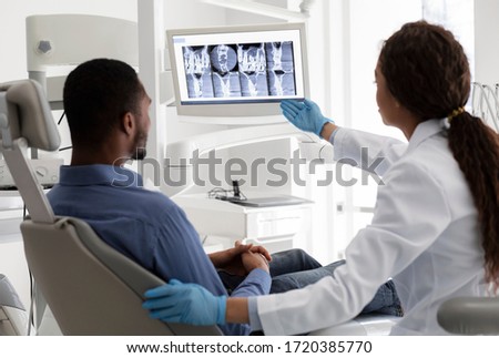 Female dentist african woman pointing at screen with xray picture, showing patient his teeth