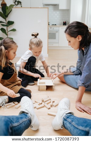Point of view photo. Father looks how mom and kids playing with wooden blocks, building simple house during isolation at home.