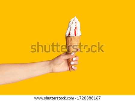 Young girl holding yummy ice cream with berry topping in waffle cone on orange background, closeup of hand