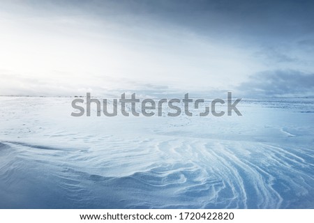 Panoramic view of the snow-covered field after a blizzard at sunset. Human tracks in a fresh snow. Ice desert. Dramatic cloudscape. Global warming theme. Lapland, Finland Royalty-Free Stock Photo #1720422820