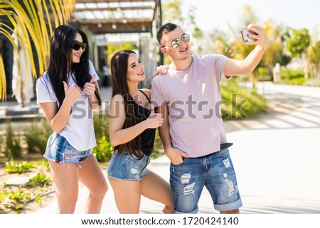 Three young friends, man is taking a self-portrait with two girls are enjoying summer vacation.