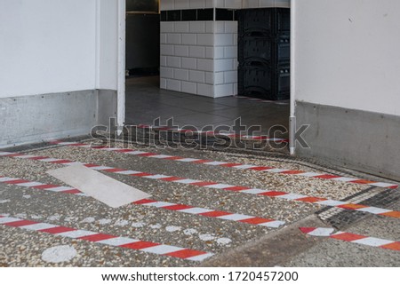 Low angle selected focus view at red and white pattern tape on the floor in front of store's entrance for customer to keep social distancing during epidemic of COVID-19 in Europe. 