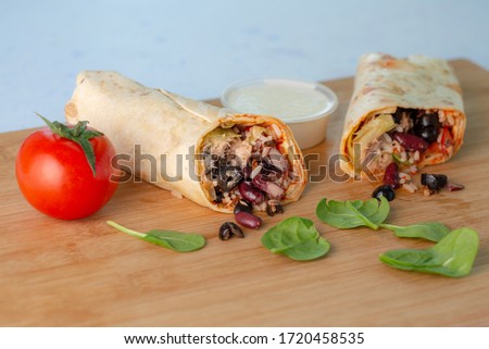 Hero angle colorful image of Mexican tortilla wraps filled with tuna meat, beans and vegetable with separated sauce bowl, tomato and spinach put on wooden desk and with light blue background.