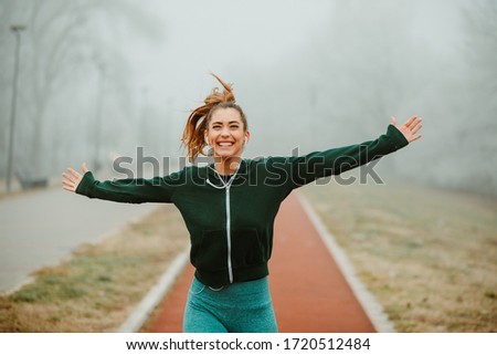 Photo of young excited woman runner with outstretching arms running outside on foggy morning.