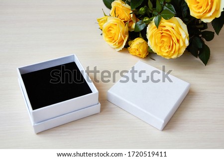 Top view for presentation. Empty box for jewelry, gift. Place for logo, sale text. Yellow roses bouquet on the table. Royalty-Free Stock Photo #1720519411