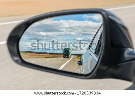 view of the outside car rearview mirror, the mirror reflects a truck driving but on the highway against the background of nature Royalty-Free Stock Photo #1720539334