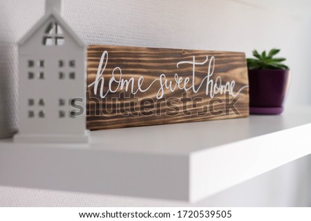 Decorative sign house sweet home from a burnt tree on a white shelf with a toy house and a flower pot, selective focus