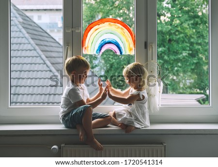 Smiling little children on background of painting rainbow on window. Photo of kids leisure at home, childcare, safety joy symbol, family life. Child Art and Creative.