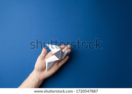 Origami pigeon  in human hand on a blue isolated background. World Peace Day concept. Close up studio photo.