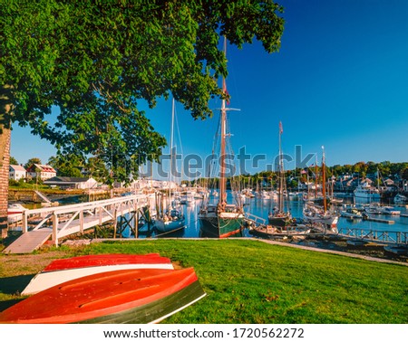 Row boats lay on grass in front of fishing and recreational boats in the harbor of Camden, Maine in the New England area of the Eastern USA.