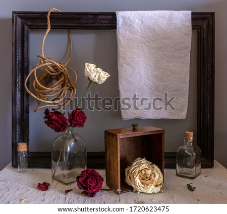Still life with dried roses, a wooden box, a picture frame, a rope, a sheet of white paper and bottles. Vintage. Interior.