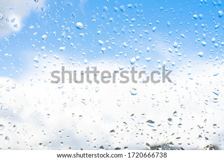 Raindrops on window glass against blue sky with white clouds