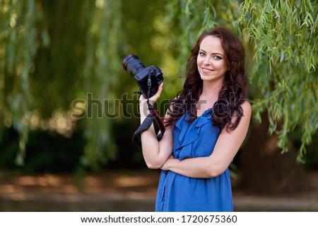 Portrait of a happy young woman 30-33 years old in the summer park. Girl with a camera. Photographer.