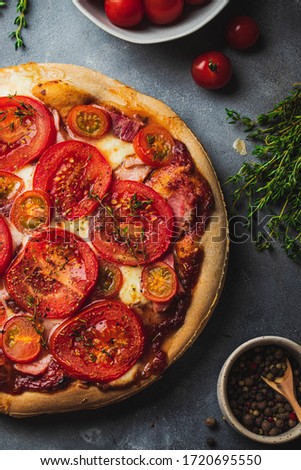 baked pizza with whole grain dough, tomato, ham, mozzarella, tomato sauce, thyme searved on gray stone background with various ingredients for cooking. flatlay. close up