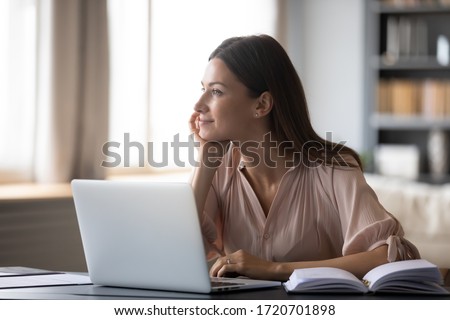 Dreamy young woman pondering ideas, sitting at desk with laptop, distracted from work, beautiful female looking in distance, taking break, dreaming or visualizing at home Royalty-Free Stock Photo #1720701898