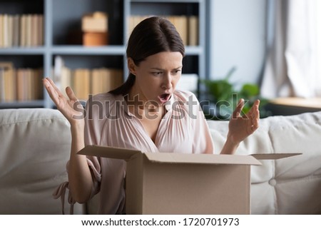 Angry shocked young woman unpacking parcel at home, dissatisfied female looking in cardboard box, wrong or damaged shopping order, bad delivery service, displeased by post shipping Royalty-Free Stock Photo #1720701973