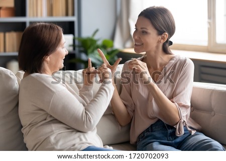 Happy adult daughter and older mother speaking sign language, having fun, sitting on sofa at home, smiling young woman and mature mum chatting, communicating, showing gestures, deaf family Royalty-Free Stock Photo #1720702093