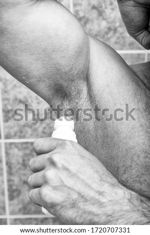 Clean and fresh. Cropped image of young shirtless man using dry deodorant while standing isolated on grey background