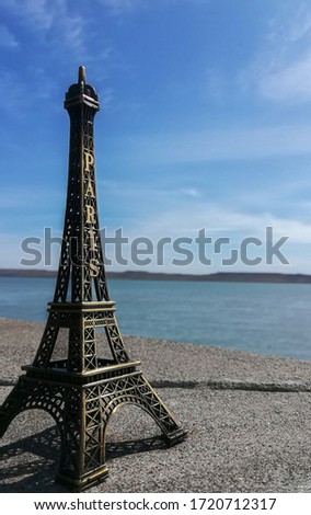 miniature eiffel tower close up with water, mountains and the sky from far out of focus