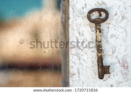 Old rusty key on the wooden door frame with broken white paint and a blurred reflection of a blue sea on a dirty glass