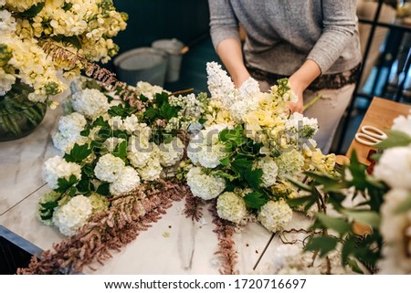 Process of making a bouquet of seasonal white flowers. Female florist making bouquet in flower shop.